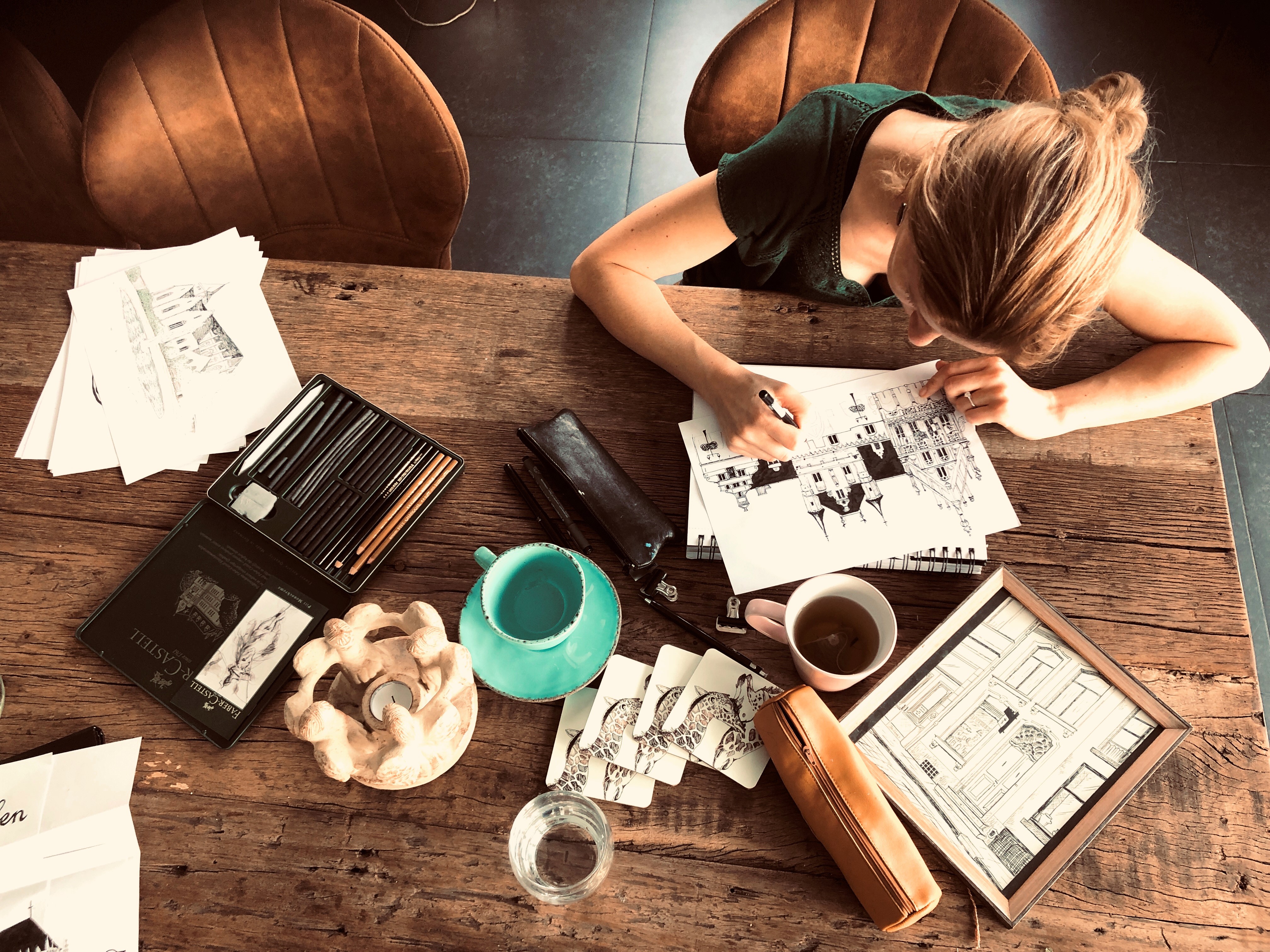 Illustrator drawing detailed cityscape at a wooden table with art materials and coffee